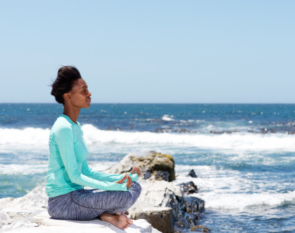 Woman meditating on rocks at the beach